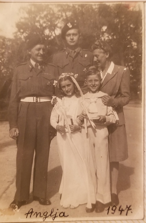 5. Aleksander, Adam, Jadwiga, Maria, Andrzej Zamoyscy, 1947 r., ze zbiorów Jadwigi Zamoyskiej Fotografia archiwalna w sepii, zrobiona w 1947 roku. Przedstawia rodzinę Zamoyskich: pierwszy z lewej mężczyzna w średnim wieku, obok niego, nieco z tyłu wysoki, młody mężczyzna -obaj ubrani w mundury 2 Korpusu Polskiego. Dalej kobieta w średnim wieku, ubrana w białą bluzkę z kołnierzem, marynarkę i spódnicę. Kobieta obejmuje dłońmi dwoje dzieci stojących z przodu – dziewczynkę i chłopca – w białych strojach „komunijnych” – dziewczynka ma długą sukienkę i wianek z kwiatów i wstążek na głowie, chłopiec spodnie i bluzę o marynarskim kroju; w rękach trzymają białe, długie świece i małe książeczki. U dołu odręczny napisy „Anglia” i „1947”. W tle wysokie drzewa i fragment szerokiej drogi.