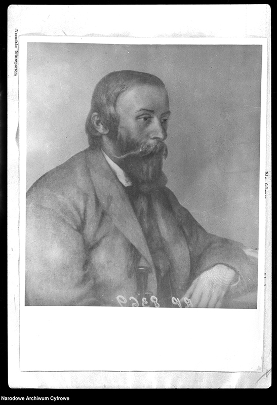 Fotografia portretu mężczyzny ukazanego w profilu, mężczyzna ma długie włosy opadające na kark, brodę i wąsy. Zarost elegancko ułożony. Ubrany w marynarkę, lewa dłoń oparta na kolanie. Wpatrzony w dal.