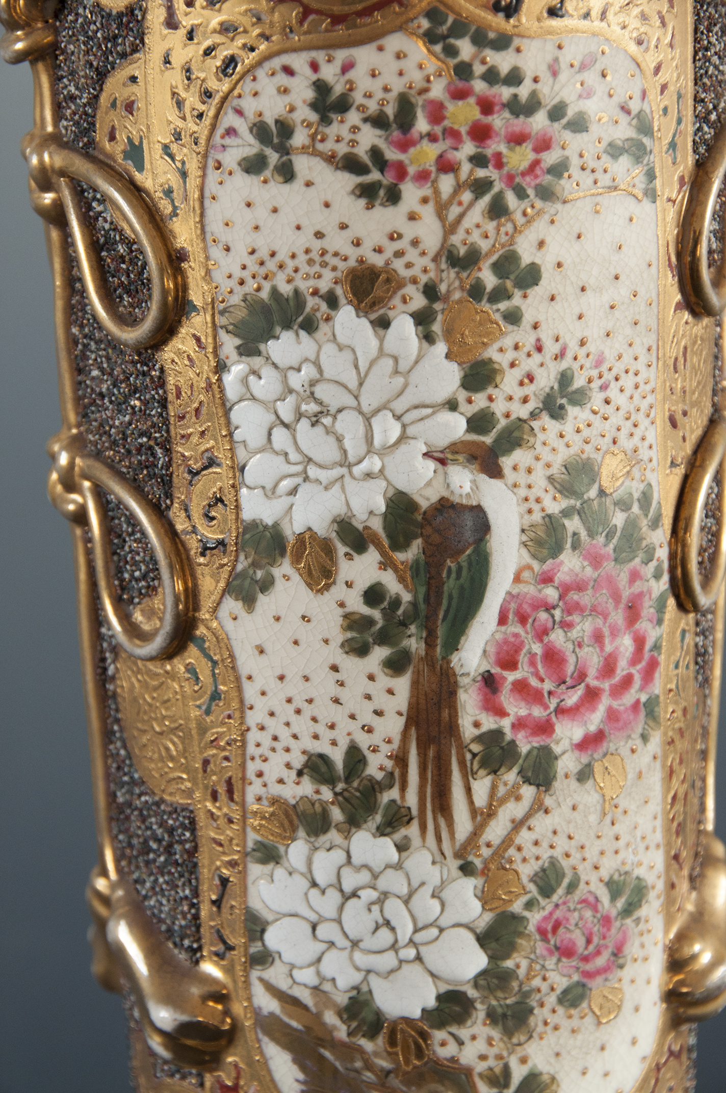 Na ceramicznym korpusie lampy naftowej bogato dekorowana złoceniami przestrzeń, w złotym ornamencie wydzielone pole wpisana dekoracja z kwiatami wiśni i piwonii oraz sroką.