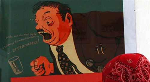 Plakat satyryczny autorstwa Ignacego Witza, 1955. Praca prezentowana w roku 2003 w Galerii Sztuki Socrealizmu Muzeum Zamoyskich w Kozłówce. Foto: PAP/ Mirosław Trembecki, https://polskieradio24.pl/130/5646/artykul/2475444,kwadratura-kultury-artysta-i-krytyk-sztuki-ignacy-witz Plakat - karykatura przedstawiający człowieka w furii, który z mównicy wykrzykuje słowa żeby mi tu nie było komenderowania. Jego zaciekłość, niemal szaleńczy obłęd jest tak wielki, że przewraca stojącą na mównicy szklankę z wodą, a oczy prawie wychodzą mu z orbit. Wąsata postać o rzadkich przetłuszczonych włosach, niemal wychodzi z płaszczyzny obrazu. Kolorystyka w czerwieniach, podkreśla dynamizm i dramatyzm całości. Czarna marynarka i biała koszula potęgują napuchniętą z gniewu, czerwoną twarz mówcy. Tło w kolorze zgaszonej, ponurej zieleni.