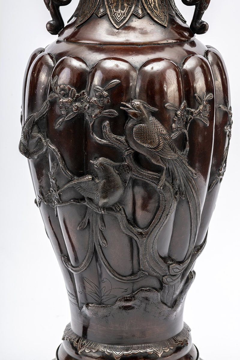 Fragment dekoracji korpusu lampy naftowej w typie dalekowschodnim, 2. połowa XIX wieku; zbiory Muzeum Zamoyskich w Kozłówce, nr inw. MPK/ZM/344 Zbliżenie na korpus lampy w ciemnobrązowym kolorze, rozszerzający się ku górze, z wypukłymi dekoracjami w postaci gałęzi kwitnącej jabłoni, z siedzącymi i fruwającymi ptakami.