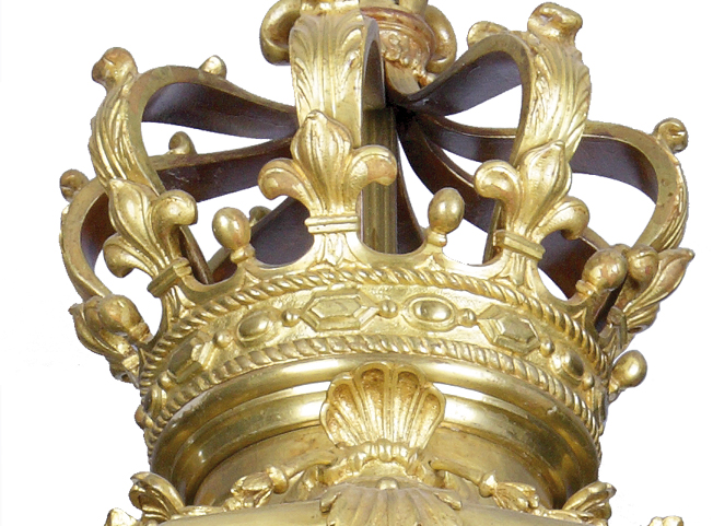 Latarnia z sieni pałacowej, detal z pełnoplastyczną koroną Fragment latarni z sieni pałacu w Kozłówce. Zbliżenie na dekorację w postaci pełnoplastycznej korony. Widoczna jest obręcz z ornamentem i pięć esowato wygiętych do góry ramion, łączących się w jednym punkcie. Przy łączeniu ramion z obręczą lilie burbońskie, pomiędzy nimi z obręczy wychodzą niewielkie owalnie zakończone pałki. W dole obręczy ornament w postaci pojedynczej muszli.