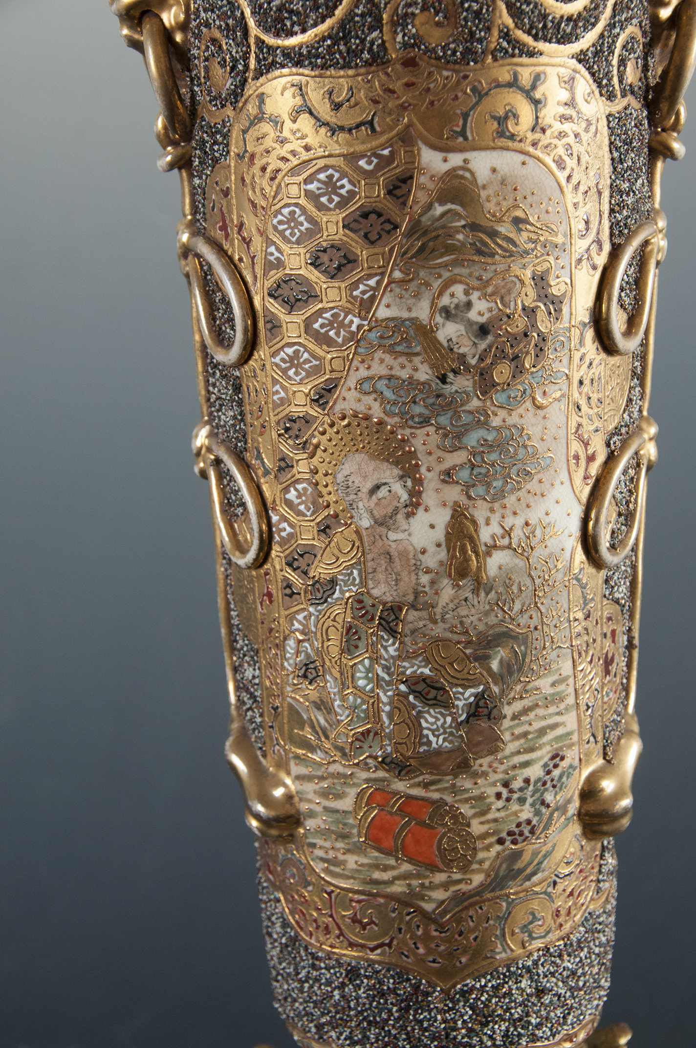 3. Dekoracja korpusu lampy, scena z japońskiej legendy o miłości Orihime i Hikoboshi; nr inw. MPK/CS/2050 Na ceramicznym korpusie lampy naftowej bogato dekorowana złoceniami przestrzeń. W polu scena ukazująca klęczącego mężczyznę trzymającego złoty przedmiot w dłoni, nad nim z chmur wyłania się pochylona w jego kierunku w popiersiu postać kobieca.