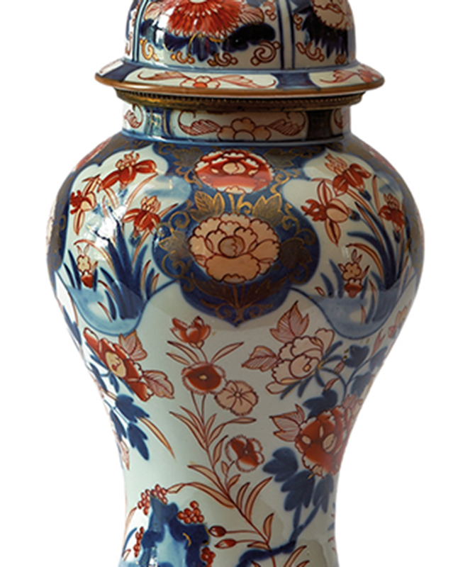 Fragment dekoracji korpusu lampy naftowej, Arita, Japonia; 2. połowa XIX wieku, porcelana; nr inw. MPK/CS/458 Fotografia kolorowa przedstawia fragment porcelanowego korpusu lampy naftowej. Na korpusie namalowane są stylizowane kwiaty lilii, goździków i chryzantem. Dekoracja w kolorystyce bieli, kobaltu, czerwieni ze złoceniami.
