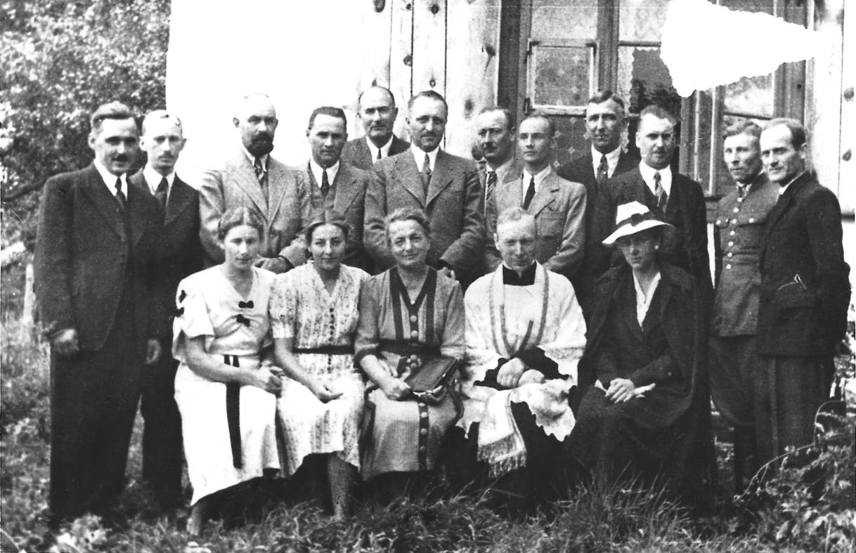 Fotografia czarno-biała. Ksiądz Stefan Wyszyński, z właścicielami majątku w Kozłówce, Jadwigą i Aleksandrem Zamoyskimi, w otoczeniu pracowników ordynacji kozłowieckiej.
