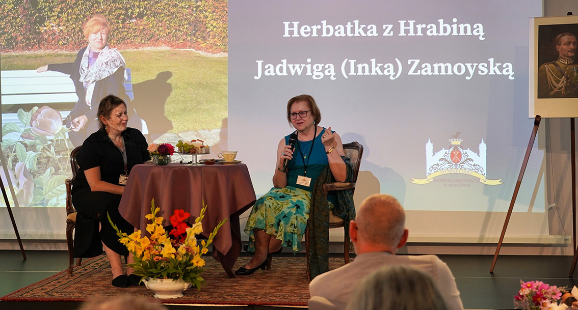 Herbatka z Hrabiną Jadwigą Inką Zamoyską Zdjęcie przedstawia wnętrze Teatralni Muzeum Zamoyskich w Kozłówce, w której na podwyższonej scenie głównej, przy scenie zasiadają dwie osoby. Jedną z nich (po prawej) jest kobieta o delikatnej urodzie, jasnych, upiętych włosach, ubrana w długą czarną sukienkę. Drugą z nich (po lewej) jest Jadwiga Inka Zamoyska, córka ostatnich właścicieli Kozłówki. Jest to starsza, zadbana kobieta o jasnych włosach, ściętych do ramion włosach, schludnie uczesanych. Ubrana jest w błękitną bluzkę na szerokich ramiączkach. Hrabina trzyma w dłoni mikrofon i ma delikatnie rozchylone usta, czym sugeruje rozmowę. W tle za kobietami znajduje się przezrocze ukazujące zdjęcie Inki z młodości na tle kozłowieckiego ogrodu, któremu towarzyszy napis „Herbatka z Jadwigą (Inką) Zamoyską”. Na pierwszym planie widać sylwetki siedzących osób tyłem – są to osoby, które słuchają wypowiedzi kobiet siedzących na scenie.