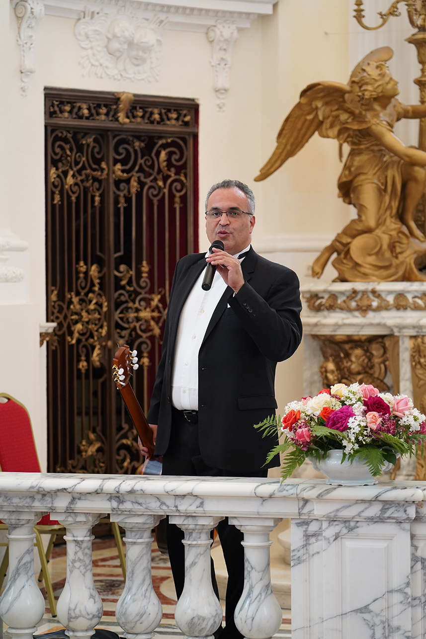 Fotografia przedstawia Mauricio Díaza Álvareza w czarnym garniturze i białej koszuli, stojącego w pałacowej kaplicy. Śpiewa do mikrofonu, a w drugiej dłoni trzyma gitarę. Przed nim znajduje się marmurowa balustrada z bukietem kolorowych kwiatów. W tle widoczne są złocona figura anioła oraz dekoracyjne, ciemne drzwi.