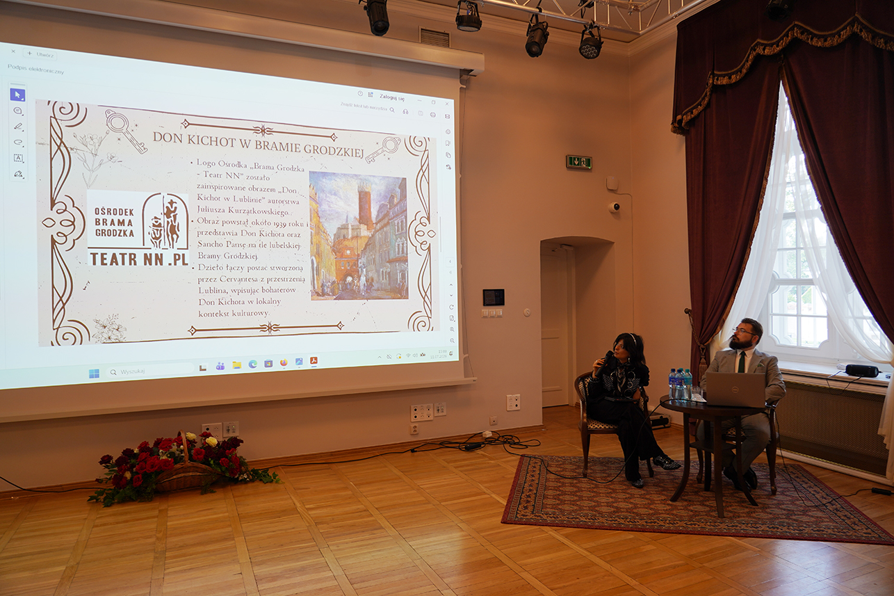 Jeden z wykładów podczas Kozłowieckich Spotkań z Kulturą Krajów Języka Hiszpańskiego. Na dużym ekranie wyświetlany jest slajd „Don Kichot w Bramie Grodzkiej”, a obok siedzą prowadzący spotkanie.
