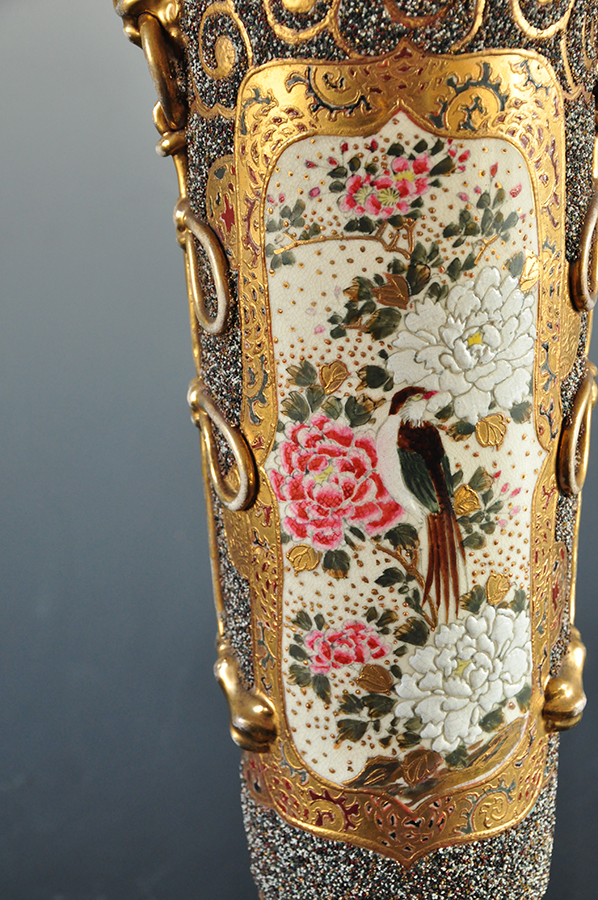 Na ceramicznym korpusie lampy naftowej bogato dekorowana złoceniami przestrzeń, w złotym ornamentem wydzielone pole wpisana dekoracja z kwiatami wiśni, piwonii i sójką.
