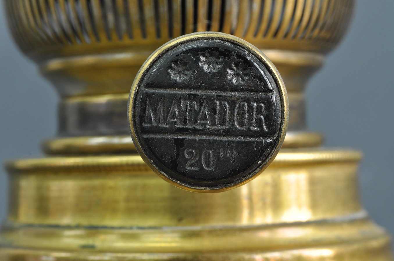 Fotografia kolorowa przedstawiająca zbliżenie pokrętła palnika lampy naftowej. Na grzybku, na ciemnym tle wyryte złotymi literami:"20''' MATADOR"