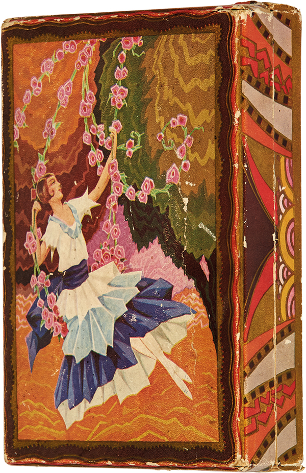 Kolorowa fotografia przedstawiająca prostopadłościenne płaskie i płytkie pudełko po słodyczach o uchylnym wieku zamocowanym przy dłuższym boku. Oklejone jest gładkim papierem z wielobarwną dekoracją w stylu art deco. Na wierzchu – ujęta falista bordiurą – kompozycja z postacią młodej kobiety siedzącej na huśtawce utworzonej z długich roślinnych i kwiatowych pędów, na tle różnokolorowych nieregularnych płaszczyzn. Dziewczyna ubrana jest w jasną bluzkę i falbaniastą spódnicę spływającą ostrymi fałdami. Przepasana jest szarfą w odcieniu granatu. Ma włosy sięgające po ucho, jasnobrązowe, z ułożonym na policzku podkręconym kosmykiem. Boki pudełka w geometryczne wzory, układające się symetrycznie dla każdej ścianki.