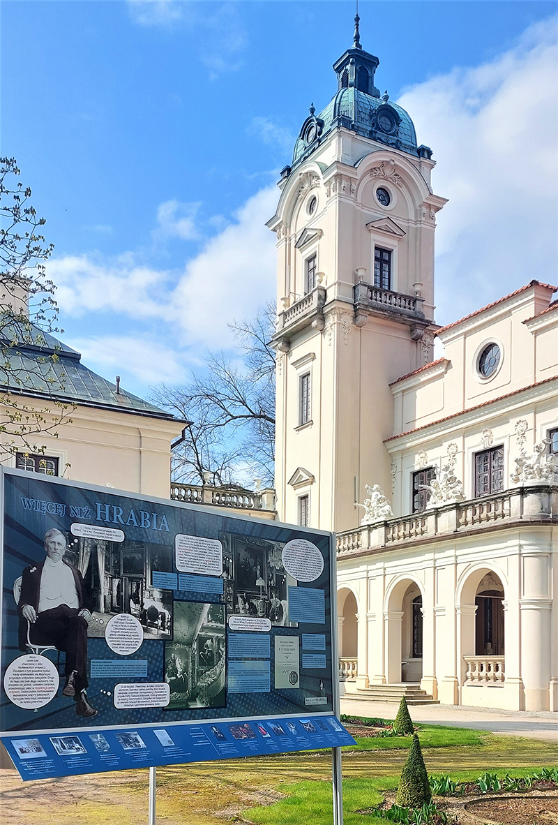 Fotografia prezentująca plenerową wystawę „Więcej niż hrabia”, na tle pałacu Zamoyskich w Kozłówce