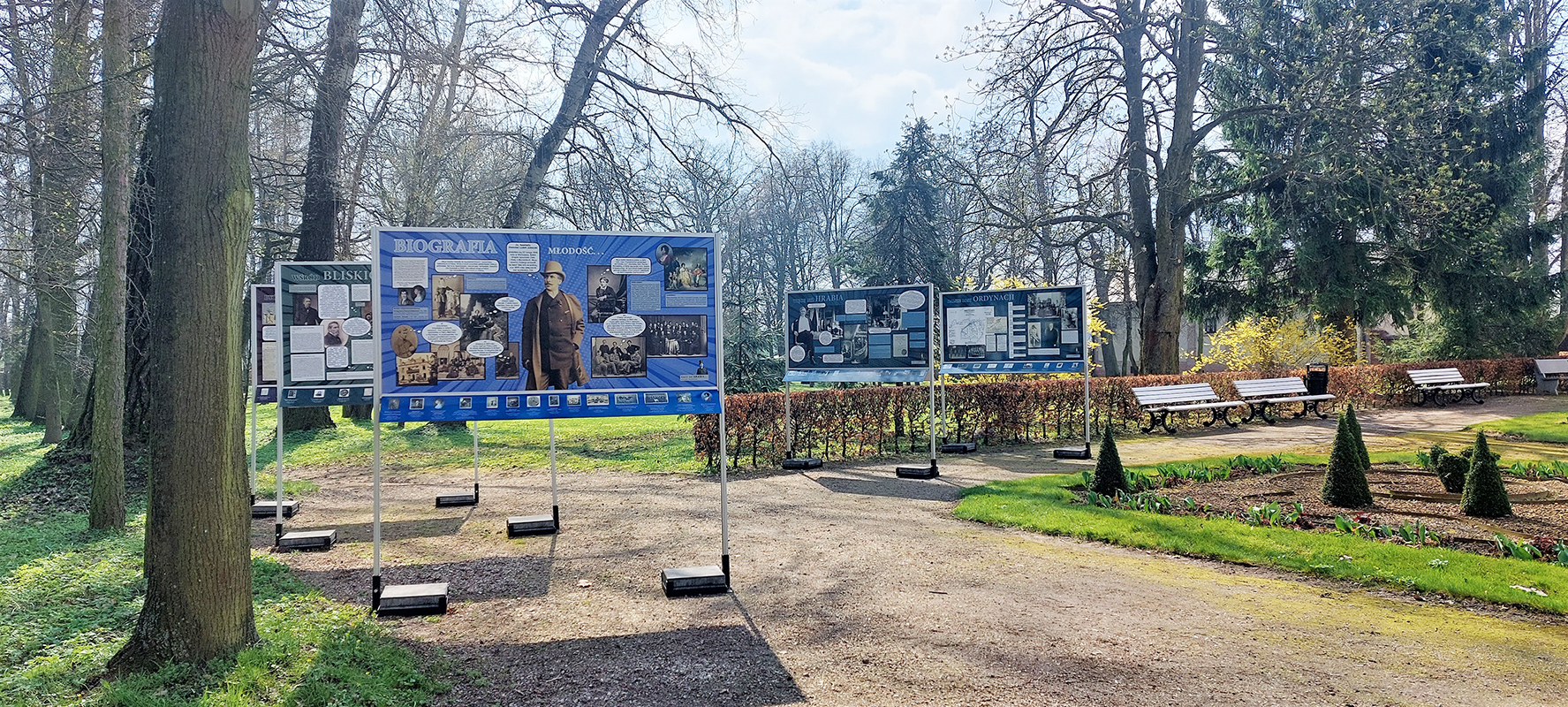 Plenerowa wystawa „Więcej niż hrabia” Na błękitnym tle, w prawym górnym i w lewym dolnym rogu odręcznie napisane listy z archiwum Konstantego Zamoyskiego, opatrzone pieczęciami odbitymi w czerwonym laku. Na górze po lewej, białymi literami napis: WIĘCEJ NIŻ HRABIA… KONSTANTY ZAMOYSKI W ARCHIWALIACH, na dole po prawej na biało BIBLIOTEKA PAŁACOWA, 12 kwietnia – 5 maja 2023