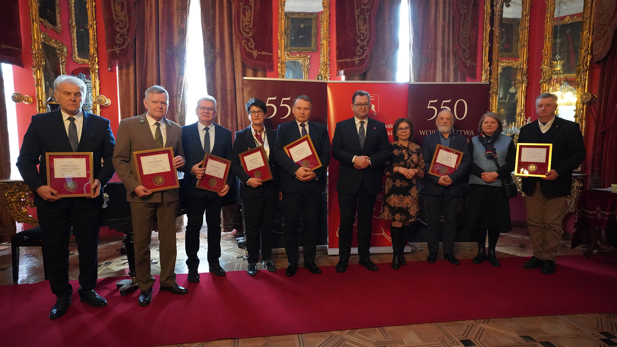 5. 4. Uroczyste Otwarcie Sezonu Kulturalnego 2024 w Lubelskich Muzeach Samorządowych Na zdjęciu widzimy grupę dziewięciu osób, które zostały uhonorowane medalami za zasługi dla Muzeum Zamoyskich w Kozłówce oraz Członka Zarządu Województwa Lubelskiego, pana Bartłomieja Bałabana. Uśmiechy i spojrzenia odznaczonych świadczą o radości i satysfakcji z tego wyróżnienia. Cała scena podkreśla znaczenie współpracy i wsparcia dla rozwoju kulturalnego regionu. W tle widoczne są charakterystyczne elementy wnętrza pałacowego, dopełniające uroczystego klimatu tego wyjątkowego wydarzenia.