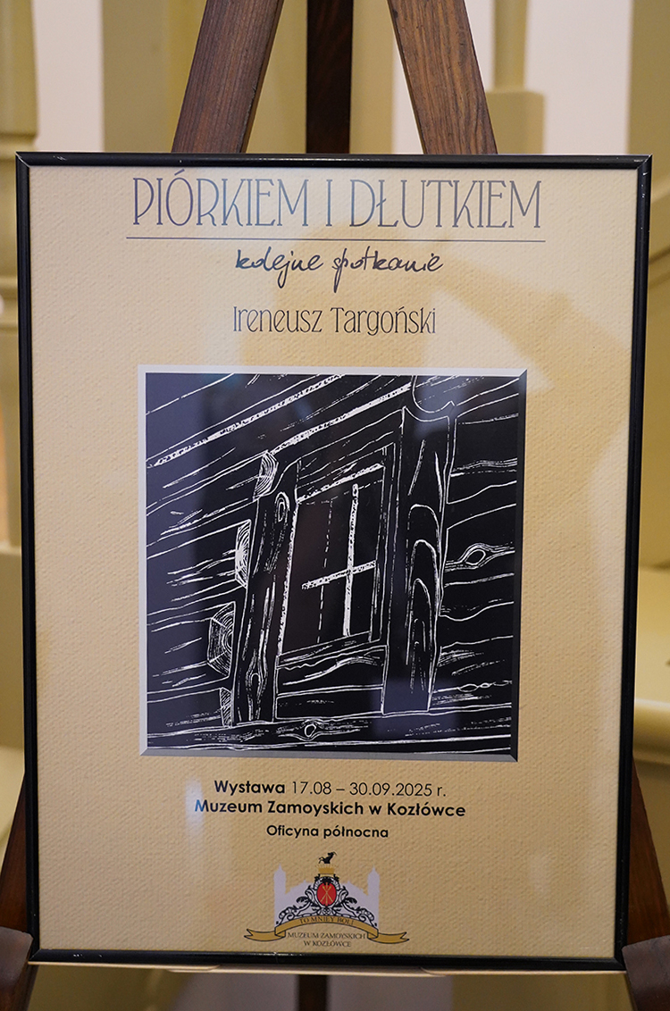 Plakat wystawy Ireneusza Targońskiego „Piórkiem i dłutkiem. Kolejne spotkanie” Zdjęcie przedstawia plakat wystawy Ireneusza Targońskiego „Piórkiem i dłutkiem. Kolejne spotkanie”, umieszczony na sztaludze, eksponowany w pomieszczeniu muzealnym. Plakat jest prostokątny, osadzony w cienkiej czarnej ramce, z tłem o jasnobeżowym kolorze przypominającym fakturę papieru czerpanego. W górnej części plakatu znajduje się tytuł w dużych, niebieskoszarych literach: „PIÓRKIEM I DŁUTKIEM” Tuż pod nim, odręcznym pismem, dopisano mniejszymi literami: „kolejne spotkanie”. Poniżej widnieje imię i nazwisko artysty: „Ireneusz Targoński”. Centralna część plakatu zawiera grafikę przypominającą linoryt – czarno-białą ilustrację przedstawiającą fragment drewnianej ściany z oknem. Kreski są wyraźne i kontrastowe, imitujące strukturę drewna. Widać drewniane bale, ramę okienną oraz szczegóły desek. Na dole plakatu zamieszczono informacje o wydarzeniu: „Wystawa 17.08 – 30.09.2025 r., Muzeum Zamoyskich w Kozłówce, Oficyna północna”. Poniżej znajduje się kolorowe logo muzeum: herb z czerwonym akcentem, wpisanym w stylizowaną grafikę pałacu, z żółtą wstęgą zawierającą nazwę instytucji: „MUZEUM ZAMOYSKICH W KOZŁÓWCE”. Plakat jest utrzymany w stonowanej, eleganckiej stylistyce. Przyciąga uwagę prostotą formy i kontrastową grafiką.